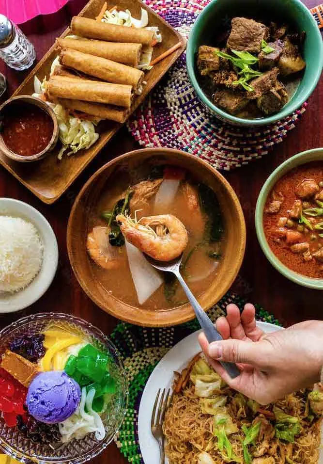 A table of Filipino food: lumpia, sinigang with shrimp, pancit, rice and halo-halo